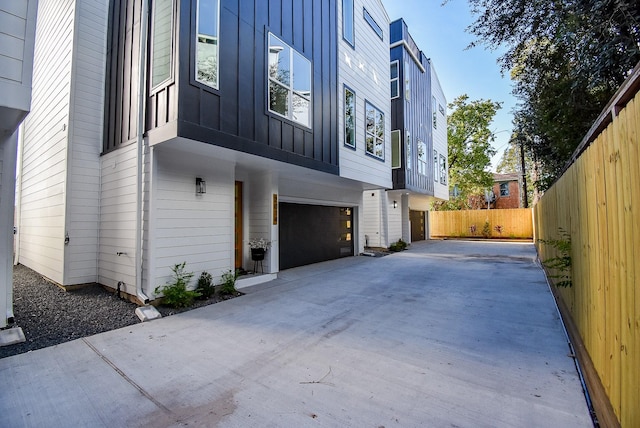 view of home's exterior with a garage, board and batten siding, concrete driveway, and fence