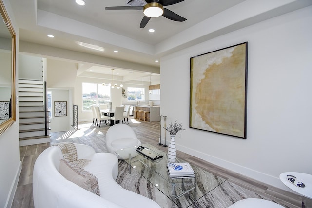 living area featuring baseboards, a tray ceiling, recessed lighting, ceiling fan with notable chandelier, and wood finished floors