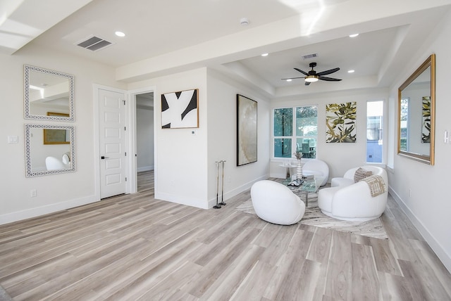 living area featuring a tray ceiling, baseboards, light wood-type flooring, and a ceiling fan