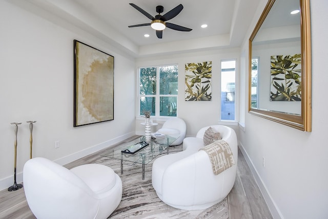 living area featuring a ceiling fan, wood finished floors, baseboards, recessed lighting, and a raised ceiling