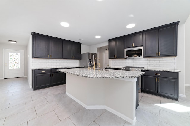 kitchen featuring light stone countertops, a center island with sink, light tile patterned floors, stainless steel appliances, and a sink