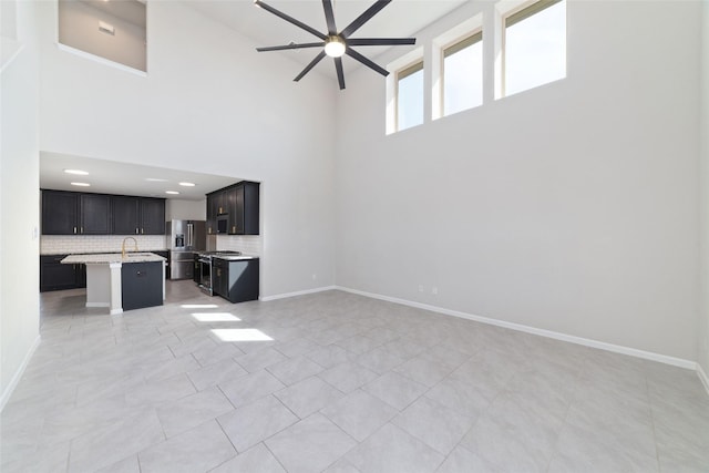 unfurnished living room featuring light tile patterned floors, a ceiling fan, baseboards, a sink, and a towering ceiling