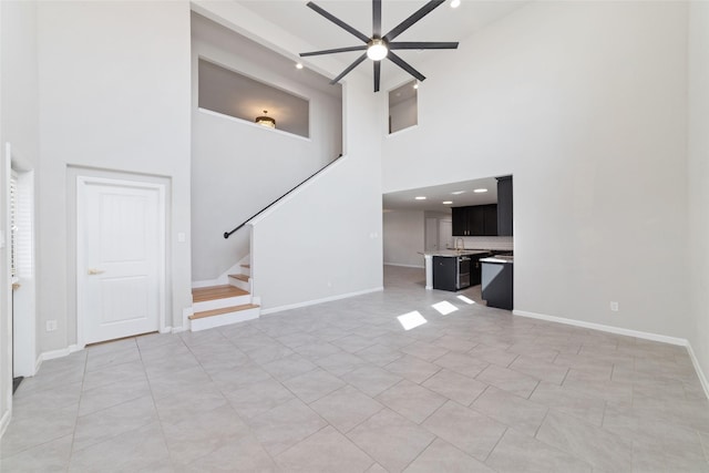 unfurnished living room featuring stairs, baseboards, and a ceiling fan