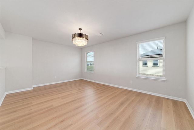 empty room featuring visible vents, a notable chandelier, light wood-style floors, and baseboards