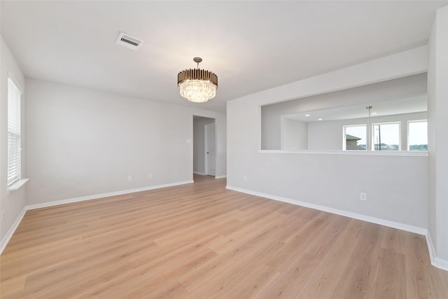 spare room with baseboards, light wood-style floors, and an inviting chandelier