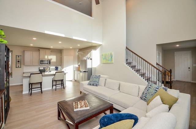 living room featuring stairs, recessed lighting, light wood-style flooring, a high ceiling, and a ceiling fan