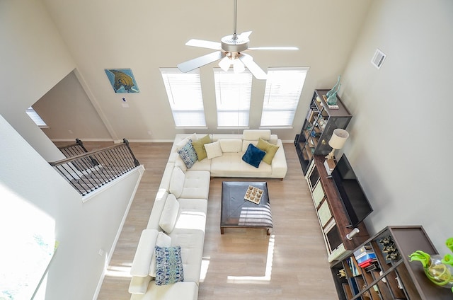 living room featuring wood finished floors, a ceiling fan, visible vents, baseboards, and a towering ceiling