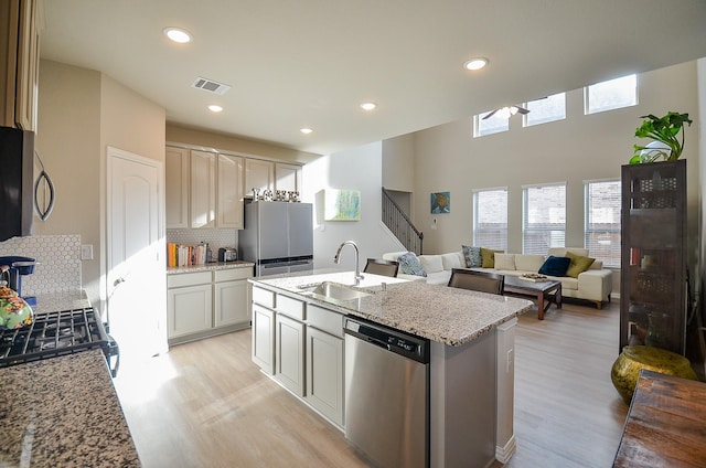 kitchen featuring visible vents, light stone counters, decorative backsplash, stainless steel appliances, and a sink