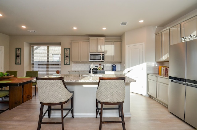 kitchen featuring a kitchen breakfast bar, light wood-style flooring, a center island with sink, and appliances with stainless steel finishes