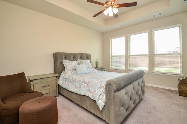 bedroom featuring visible vents, a raised ceiling, light colored carpet, and multiple windows