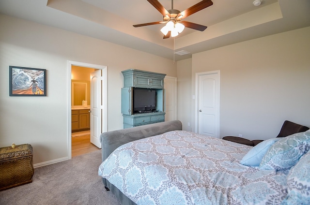 bedroom with light carpet, a raised ceiling, ensuite bath, baseboards, and ceiling fan