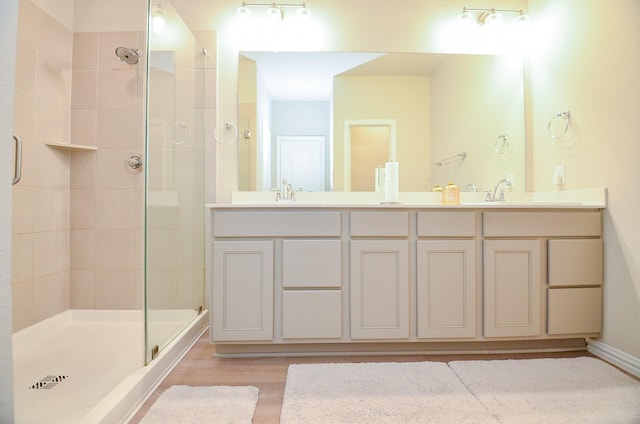 bathroom featuring double vanity, wood finished floors, tiled shower, and a sink