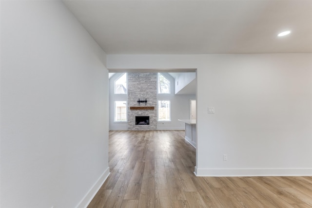 unfurnished living room featuring light wood-type flooring, baseboards, lofted ceiling, and a fireplace