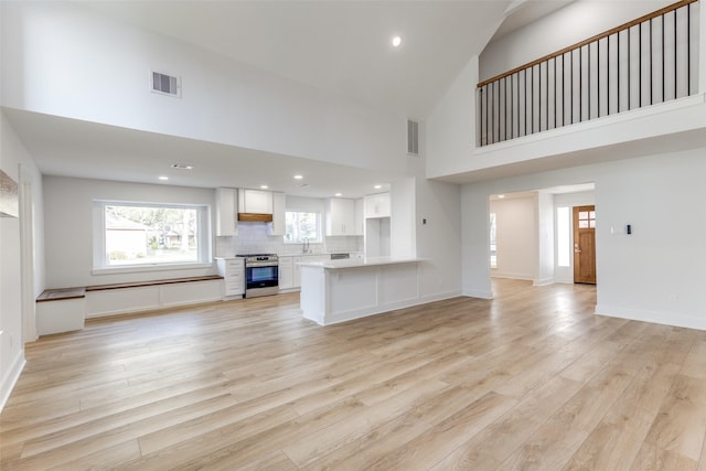 unfurnished living room with visible vents, light wood-style flooring, high vaulted ceiling, and baseboards