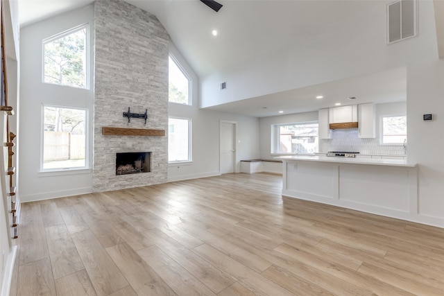 unfurnished living room with light wood-type flooring, visible vents, high vaulted ceiling, and a healthy amount of sunlight