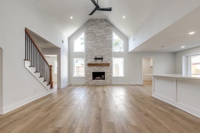 unfurnished living room with light wood-type flooring, high vaulted ceiling, baseboards, ceiling fan, and stairs