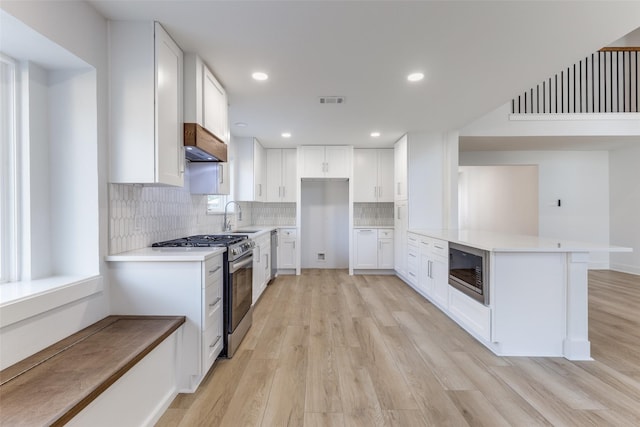 kitchen with light wood-style flooring, a sink, range hood, stainless steel appliances, and a peninsula