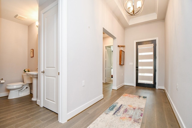 foyer with a chandelier, a tray ceiling, baseboards, and wood finished floors