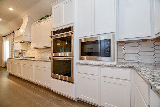 kitchen featuring tasteful backsplash, premium range hood, recessed lighting, stainless steel appliances, and white cabinetry