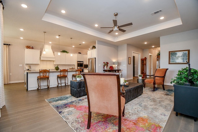 living area with a tray ceiling, visible vents, and a ceiling fan