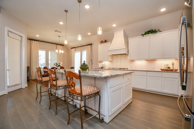 kitchen with visible vents, a sink, custom range hood, white cabinetry, and a kitchen breakfast bar