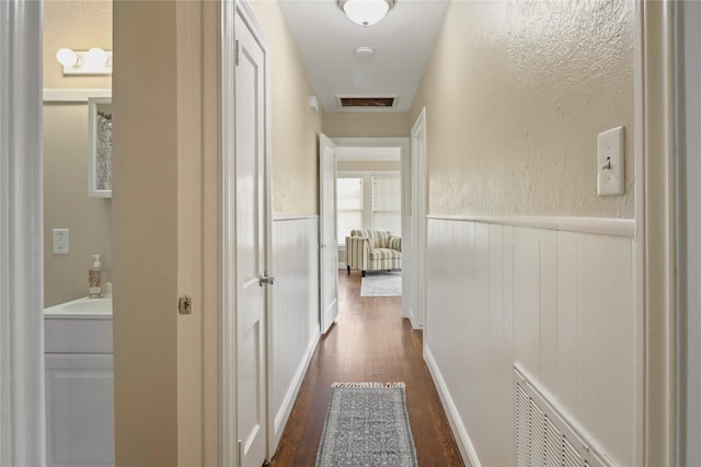 hall featuring dark wood-type flooring, visible vents, and wainscoting