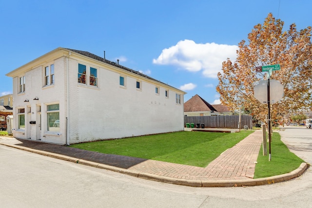 view of side of home with a yard, fence, and brick siding