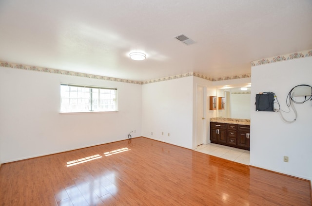 unfurnished bedroom featuring light wood finished floors, visible vents, connected bathroom, and baseboards