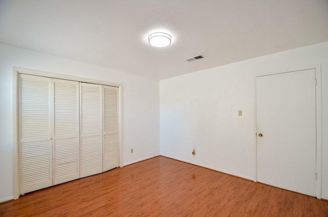 unfurnished bedroom with wood finished floors, visible vents, a closet, and baseboards