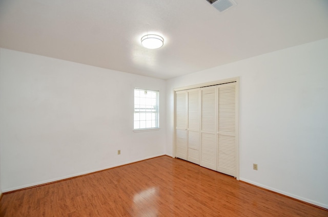 unfurnished bedroom with wood finished floors, visible vents, a closet, and baseboards