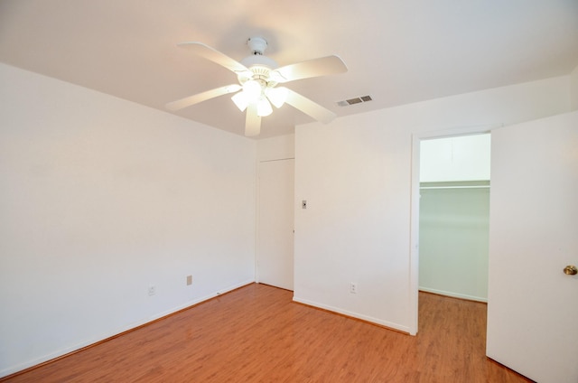 unfurnished bedroom with visible vents, a walk in closet, baseboards, light wood-style floors, and a closet