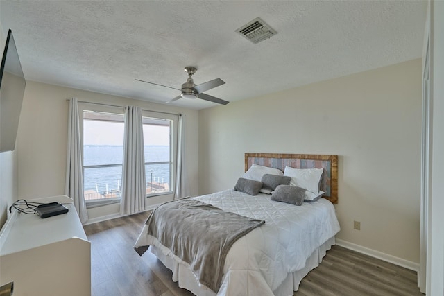 bedroom featuring visible vents, a textured ceiling, wood finished floors, baseboards, and ceiling fan