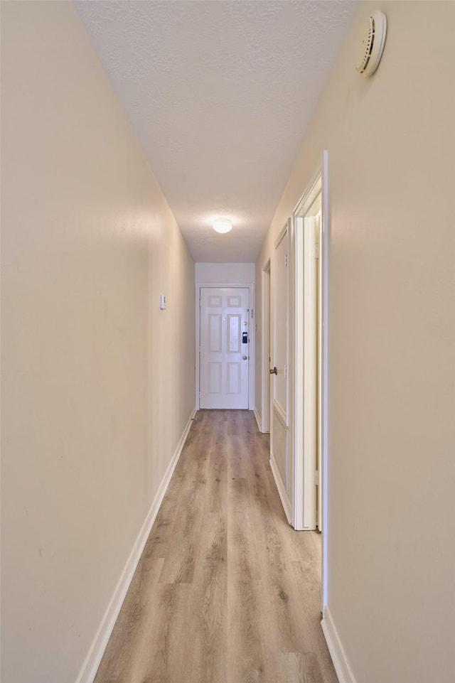 hall with light wood-style flooring, a textured ceiling, and baseboards