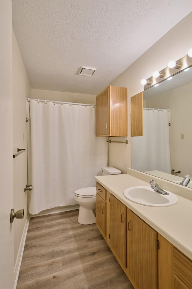 full bath with visible vents, toilet, a textured ceiling, wood finished floors, and vanity