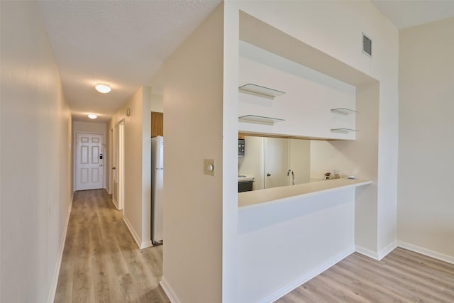 hallway with light wood finished floors, visible vents, baseboards, a textured ceiling, and a sink