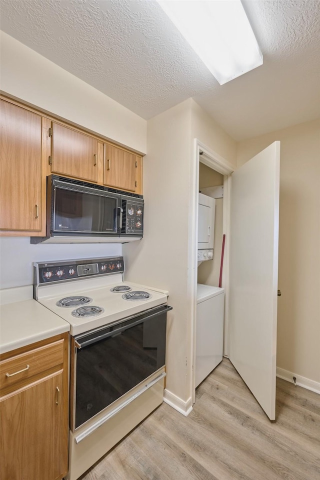 kitchen featuring black microwave, light countertops, light wood-style flooring, stacked washing maching and dryer, and white electric range