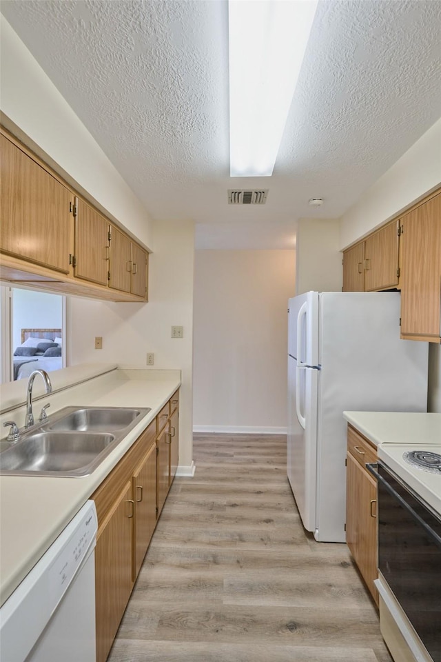 kitchen with white appliances, light wood-style floors, visible vents, and a sink