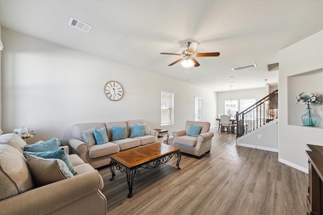 living area featuring ceiling fan with notable chandelier, stairs, wood finished floors, and visible vents