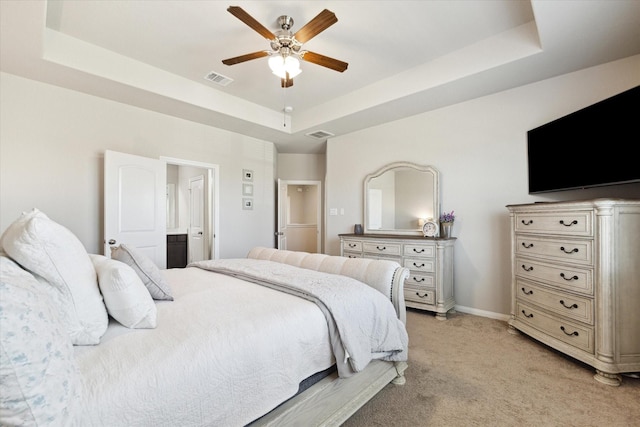 bedroom with light carpet, a tray ceiling, connected bathroom, baseboards, and ceiling fan