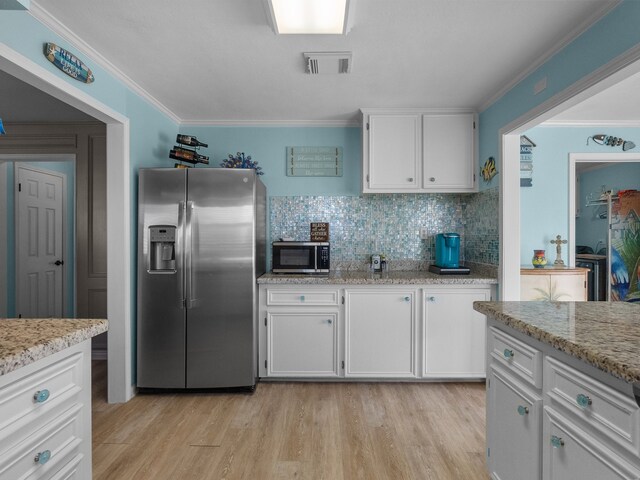 kitchen with visible vents, ornamental molding, light wood-style floors, appliances with stainless steel finishes, and white cabinetry