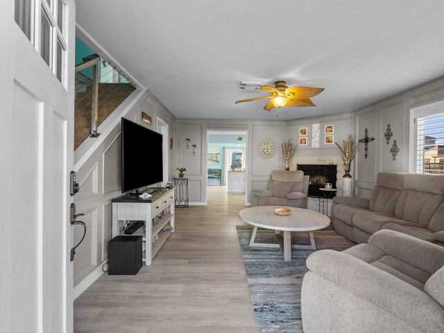 living room with light wood finished floors, visible vents, ceiling fan, a fireplace, and a decorative wall