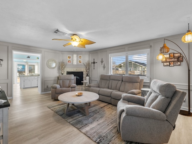 living area with light wood finished floors, ceiling fan, a fireplace, and a decorative wall