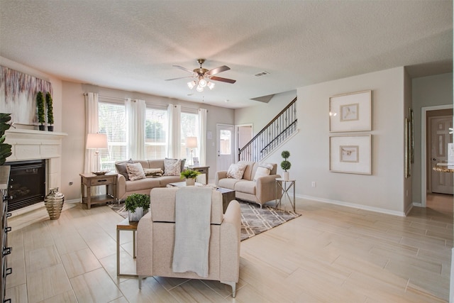 living room featuring visible vents, baseboards, stairway, a glass covered fireplace, and a ceiling fan