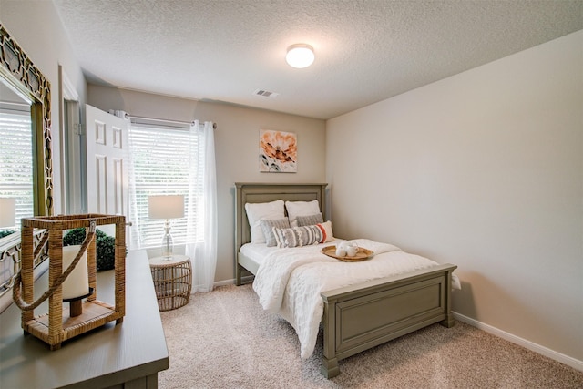 bedroom with visible vents, baseboards, light colored carpet, and a textured ceiling