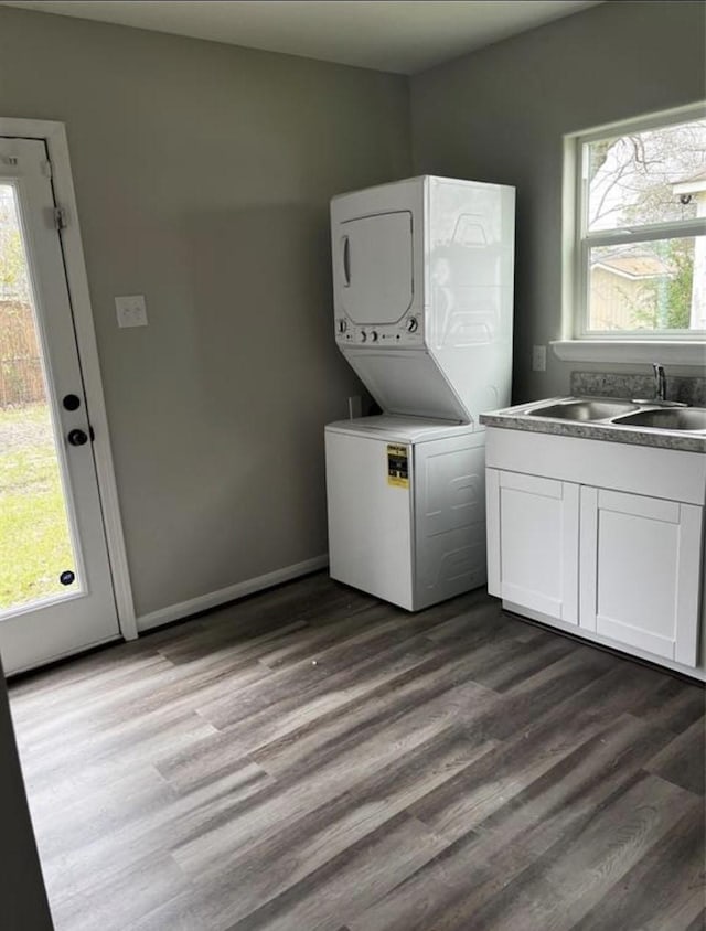 clothes washing area with dark wood-style floors, plenty of natural light, stacked washer / drying machine, and a sink