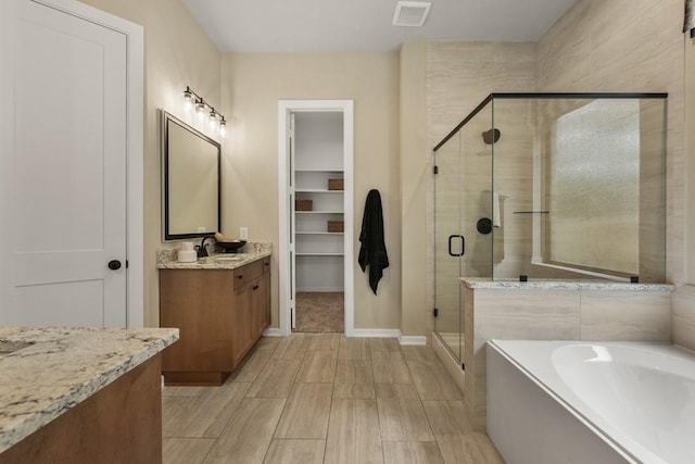 bathroom with visible vents, a walk in closet, a garden tub, a shower stall, and vanity