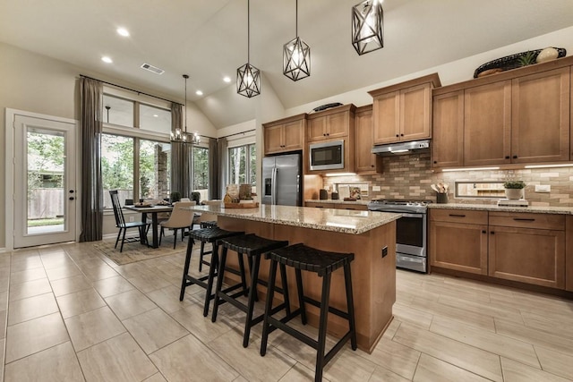 kitchen featuring brown cabinets, under cabinet range hood, appliances with stainless steel finishes, tasteful backsplash, and a center island