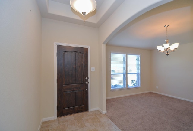 entrance foyer with arched walkways, light tile patterned flooring, baseboards, light colored carpet, and a chandelier