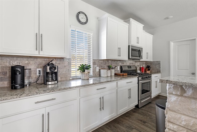 kitchen featuring light stone countertops, dark wood finished floors, stainless steel appliances, white cabinetry, and backsplash