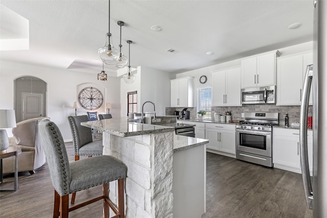 kitchen with a kitchen bar, tasteful backsplash, dark wood finished floors, white cabinetry, and stainless steel appliances